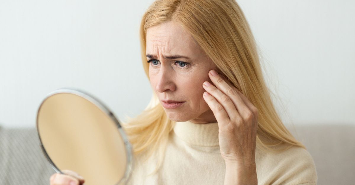 Frau betrachtet sich kritisch im Spiegel, den sie in der Hand hält.