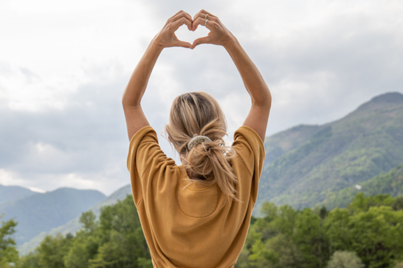 Frau in der Natur, die Yoga macht und mit den Händen ein Herz formt